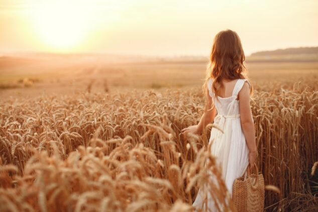 Child in a summer wheat field. Little girl in a cute white dress.